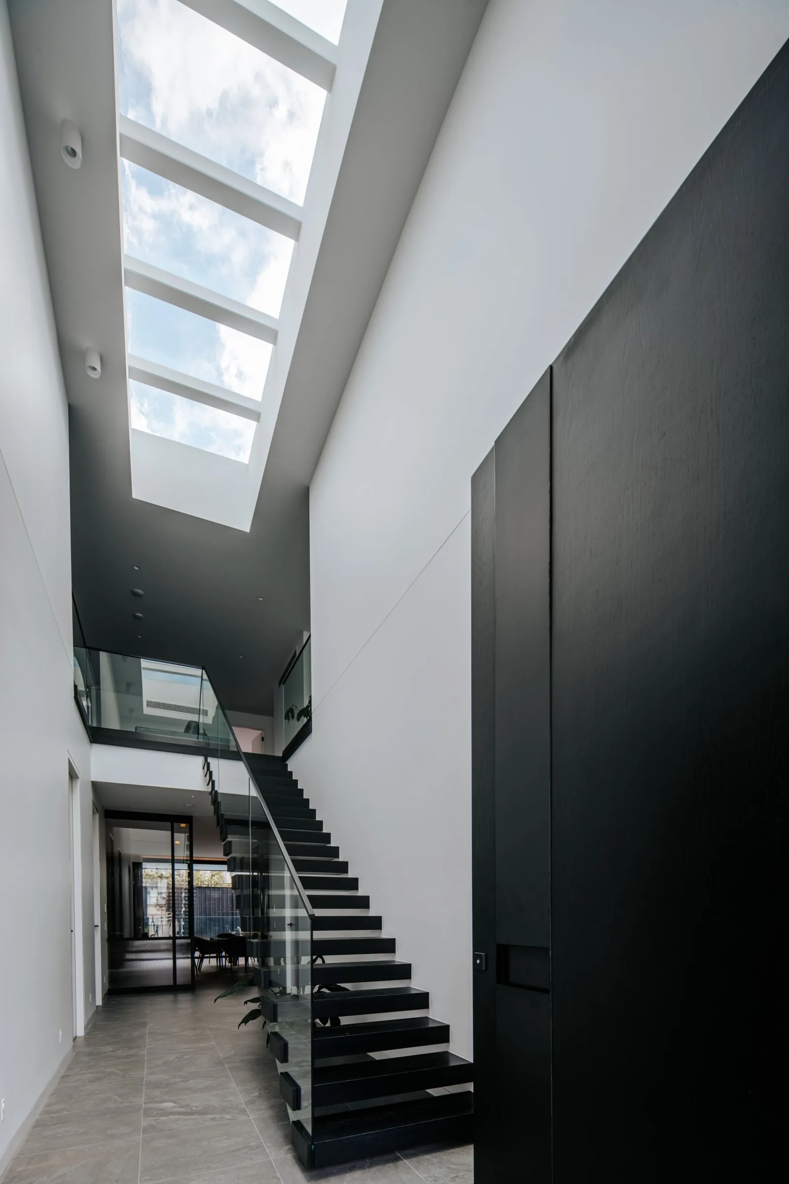 Black stair rising through a skylit void