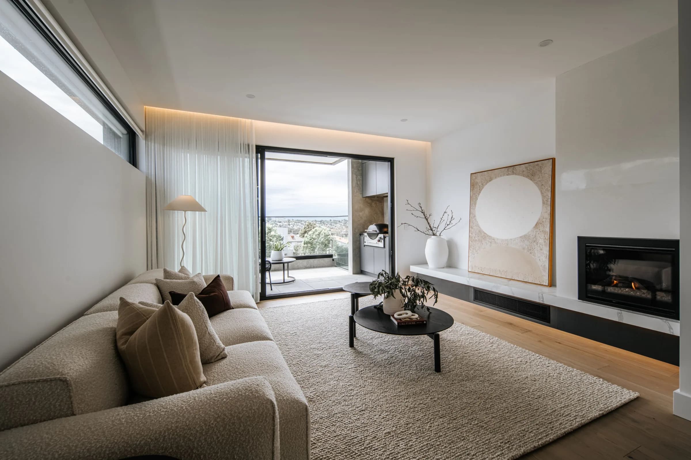 Neutral-toned lounge with in-wall fireplace and sheer curtains