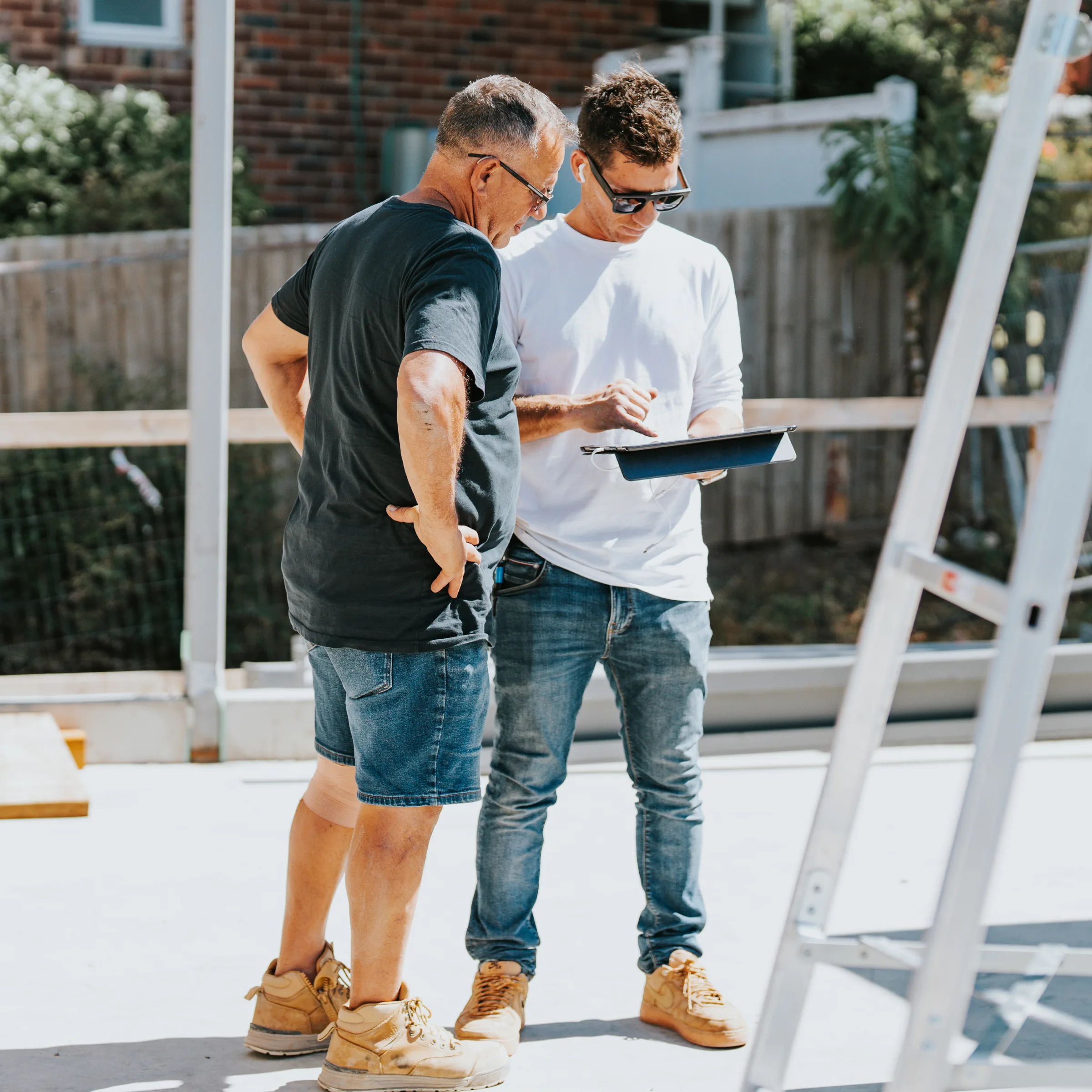 Two carpenters comparing notes beside a ladder on site