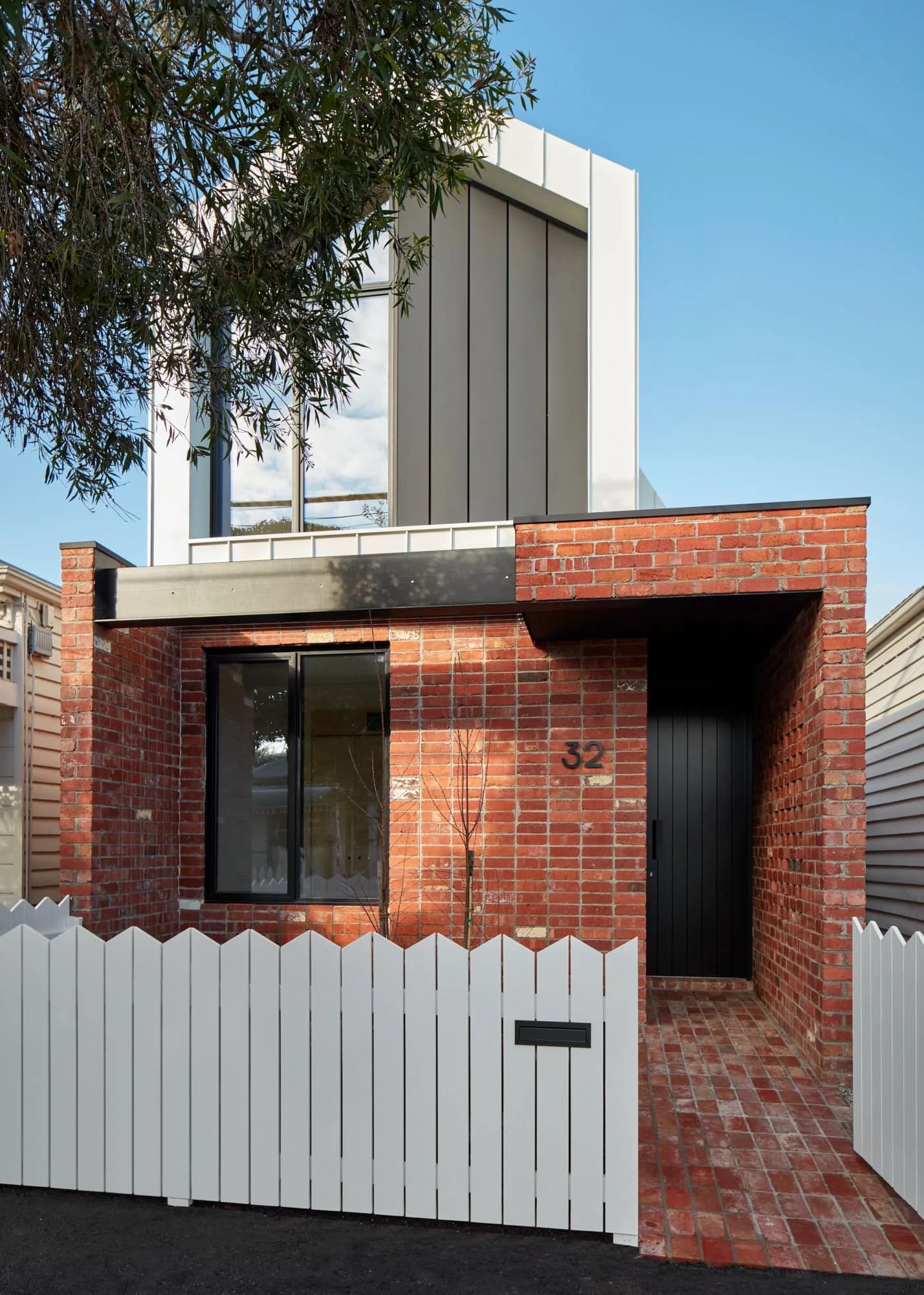 Street view of the red brick addition beside the original white picket fence