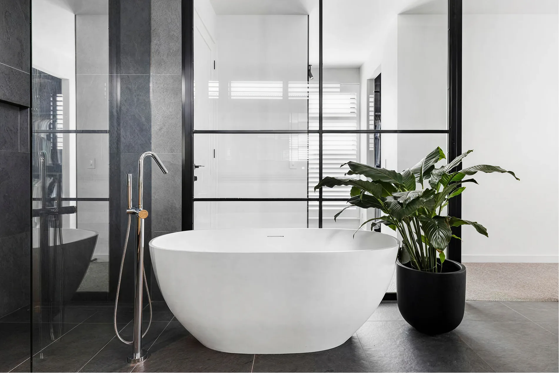 Black-framed bathroom with white freestanding tub and plant