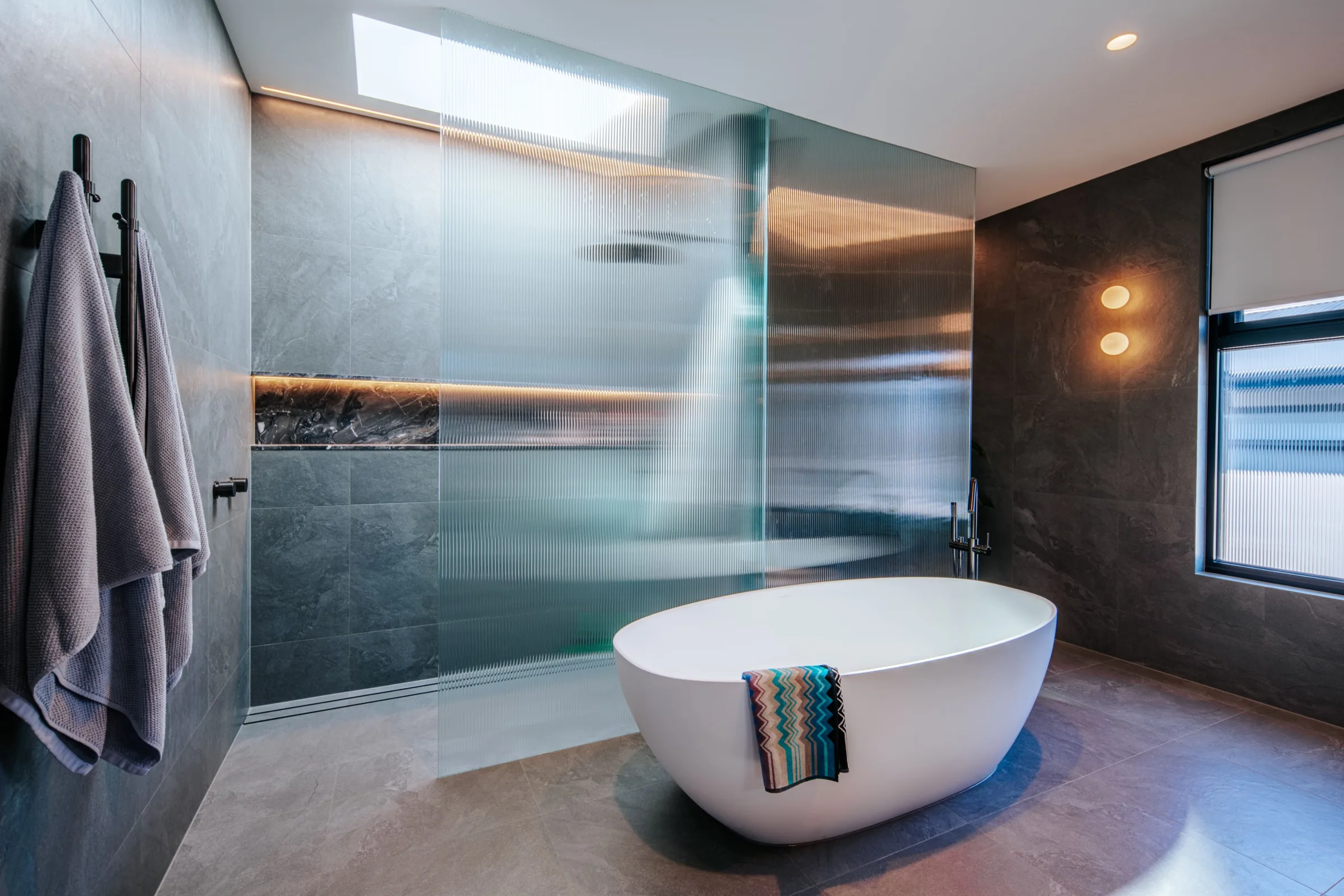 Dark stone bathroom with freestanding tub under a skylight