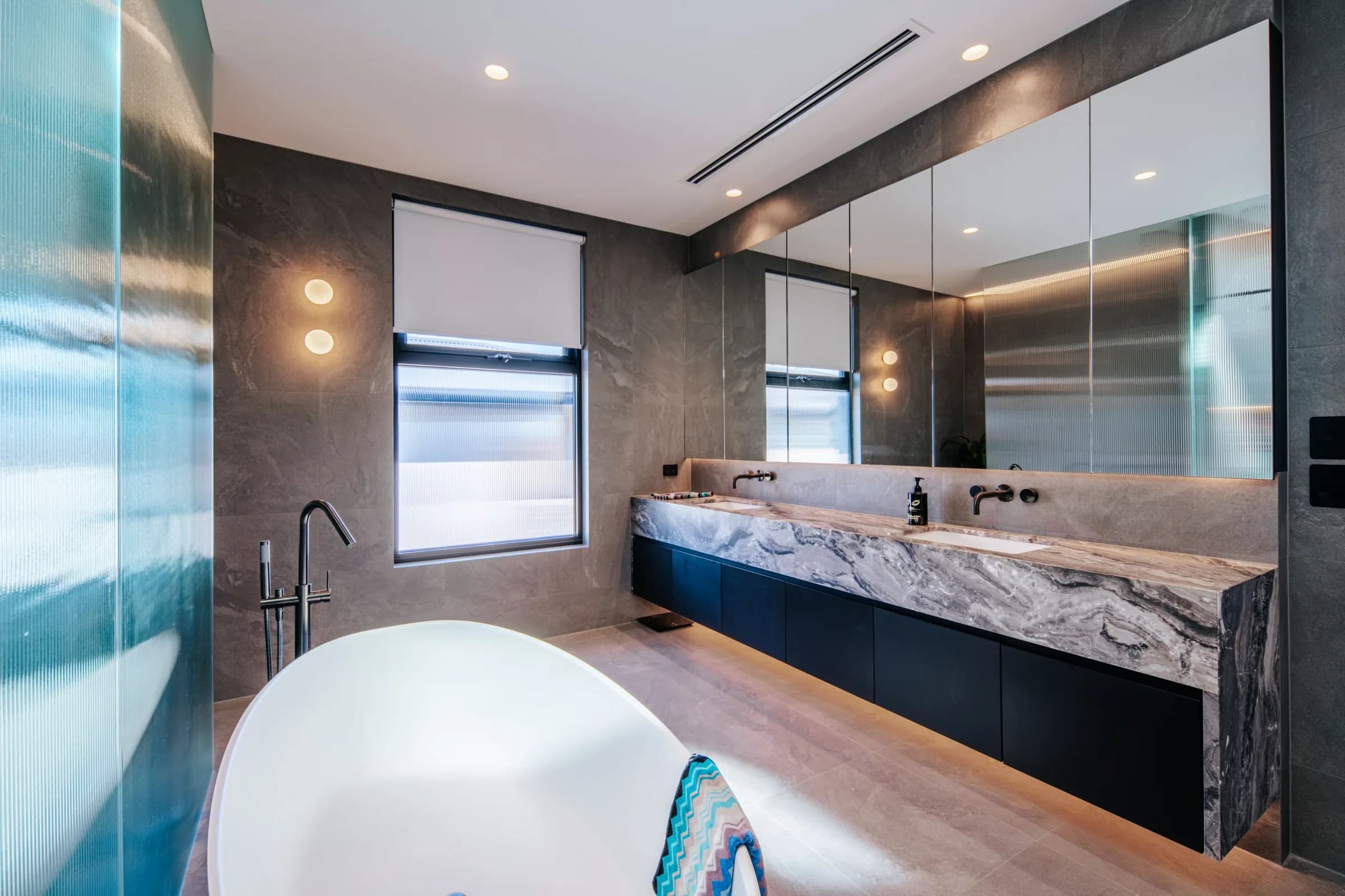 Marble vanity in a charcoal bathroom with backlit mirror